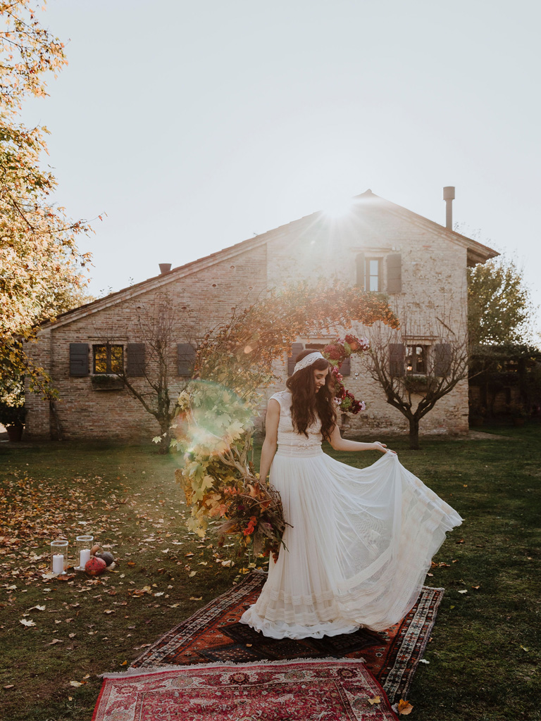Una sposa davanti a un arco floreale a mezzaluna durante un matrimonio autunnale e bohémien